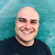 Himanshu Mehru, smiling in front of a weathered teal barn wall