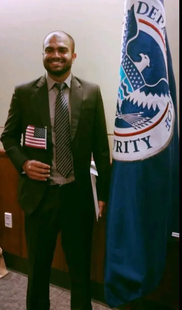 Himanshu Mehru in a suit holding a small American flag at his naturalization ceremony in 2015