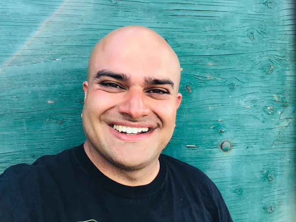 Himanshu Mehru smiling in front of a weathered teal barn wall